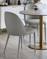 A sleek, round dining table with a gold base paired with modern light gray, ribbed upholstered chairs.