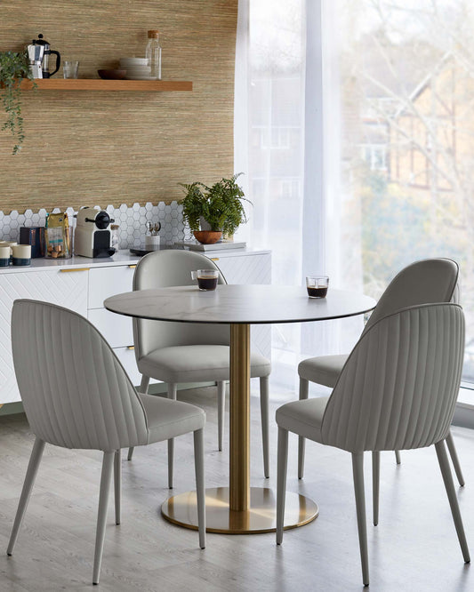 A round table with a marble top and a gold base, surrounded by four sleek, gray upholstered chairs with ribbed detailing.