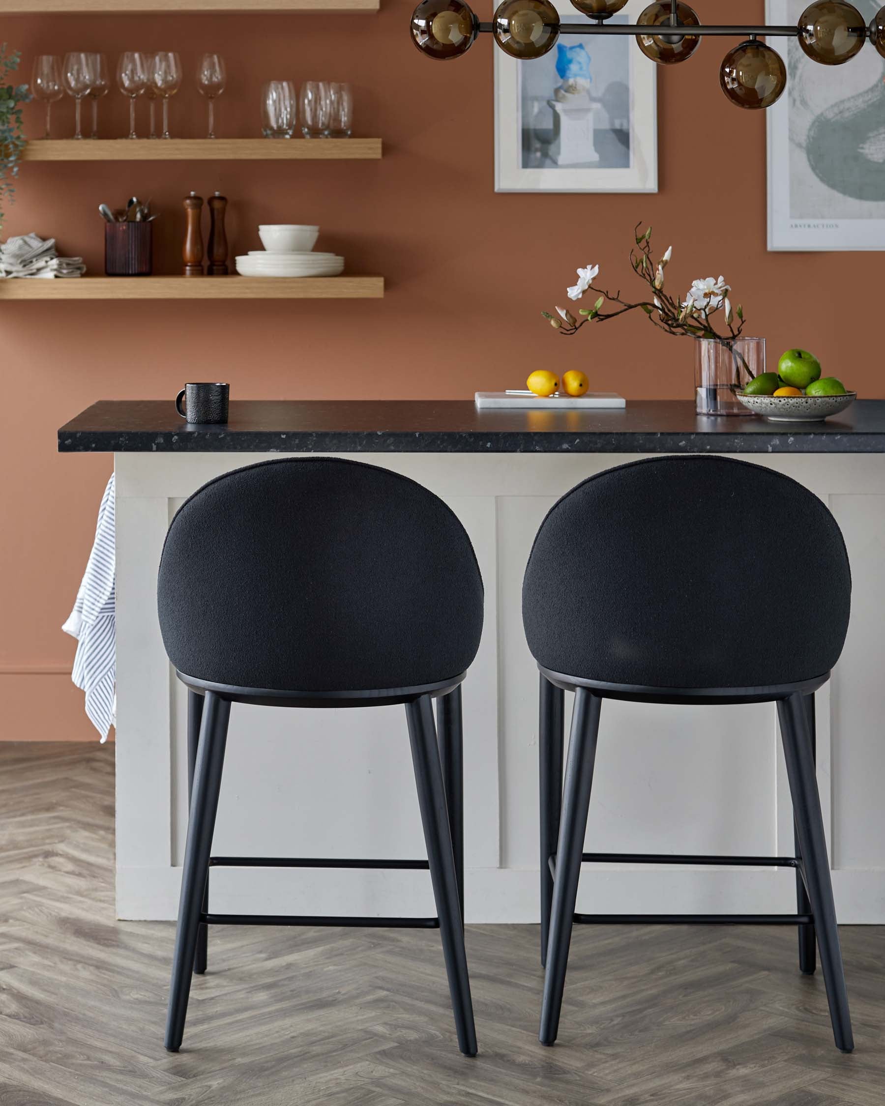 Two modern black bar stools with rounded backs, paired with a sleek kitchen island in a warm, brown-toned setting.