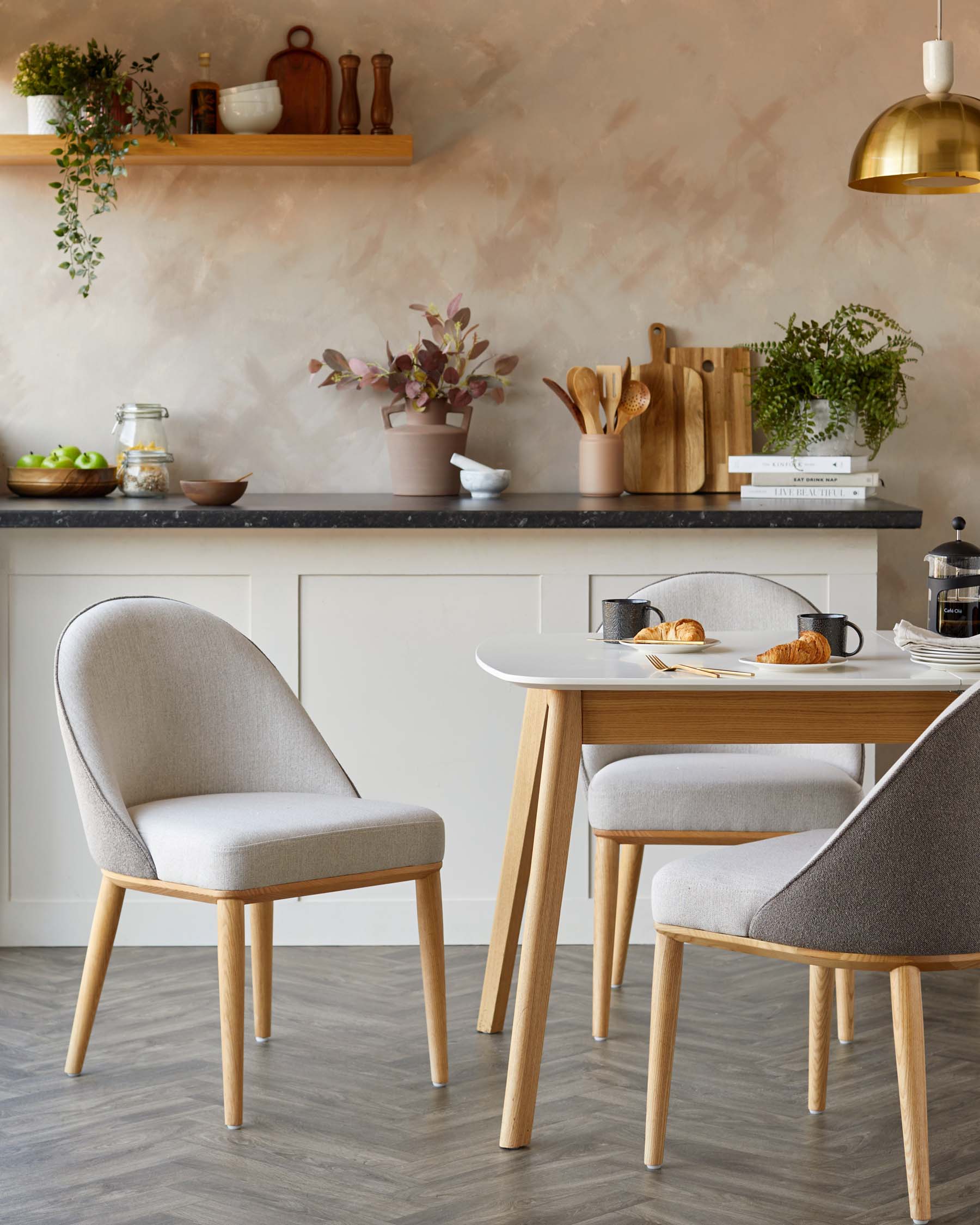 Modern dining set featuring a rounded table with wooden legs and upholstered chairs in neutral tones, perfect for a cozy kitchen.