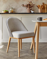 A modern gray upholstered chair with wooden legs, placed beside a stylish table in a cozy kitchen setting.