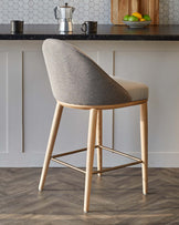 Modern bar stool with a curved back, light wood legs, and a two-tone fabric seat, set against a stylish kitchen backdrop.