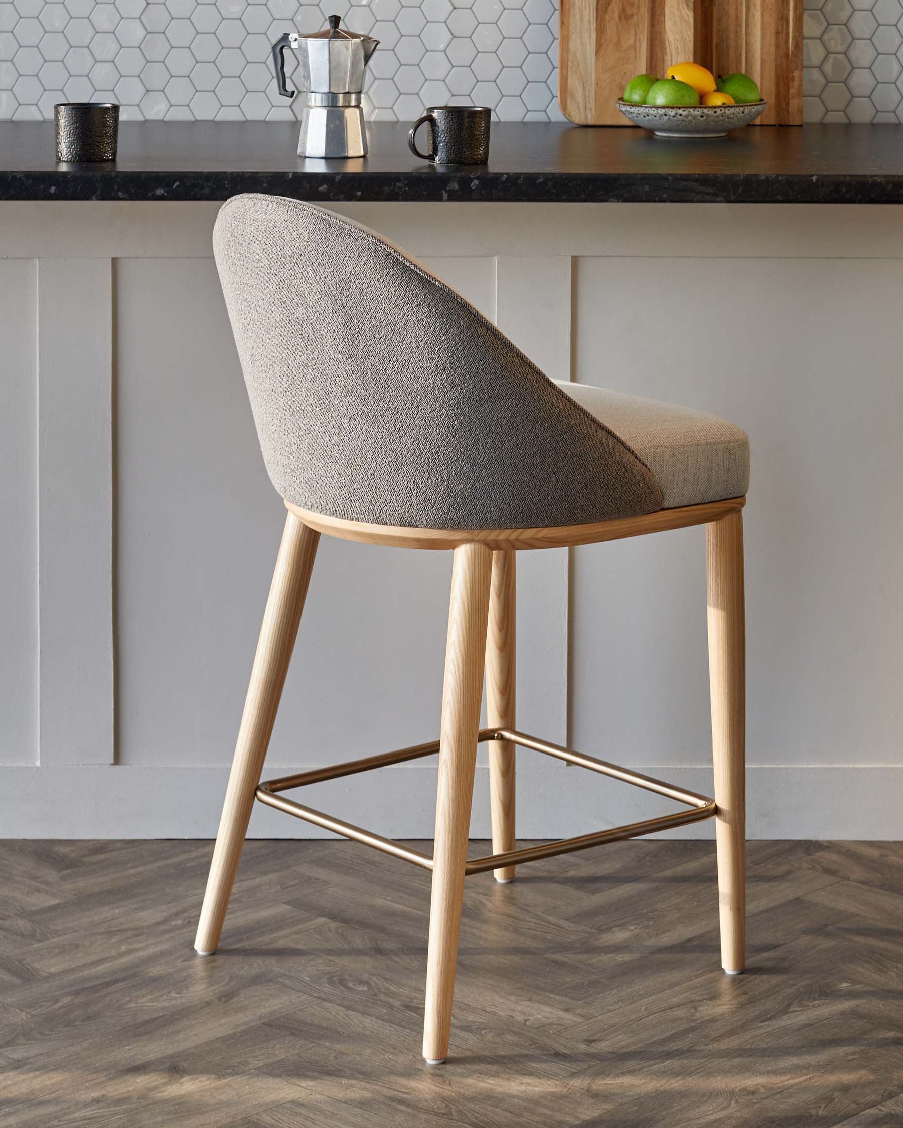 Modern bar stool with a curved back, light wood legs, and a two-tone fabric seat, set against a stylish kitchen backdrop.