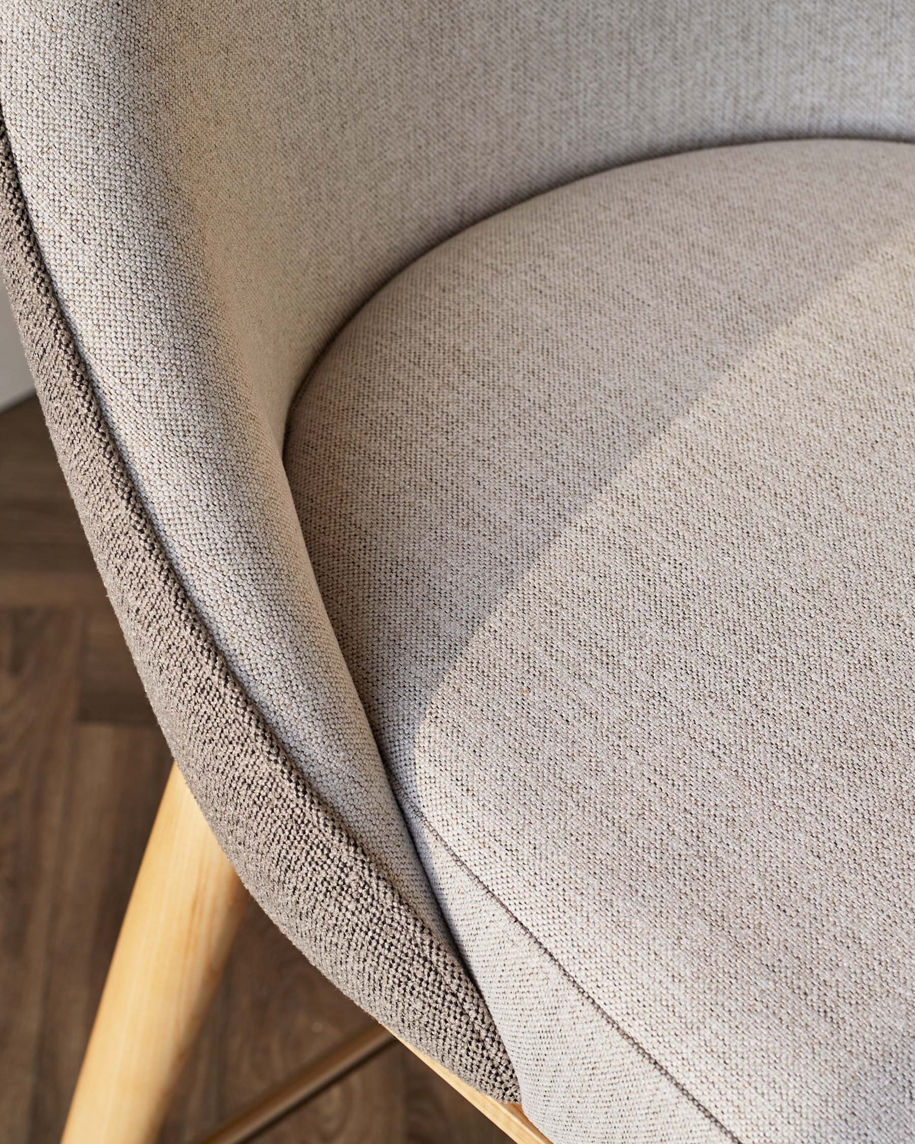 Close-up of a stylish chair featuring textured beige fabric and smooth wooden legs, highlighting contemporary design.