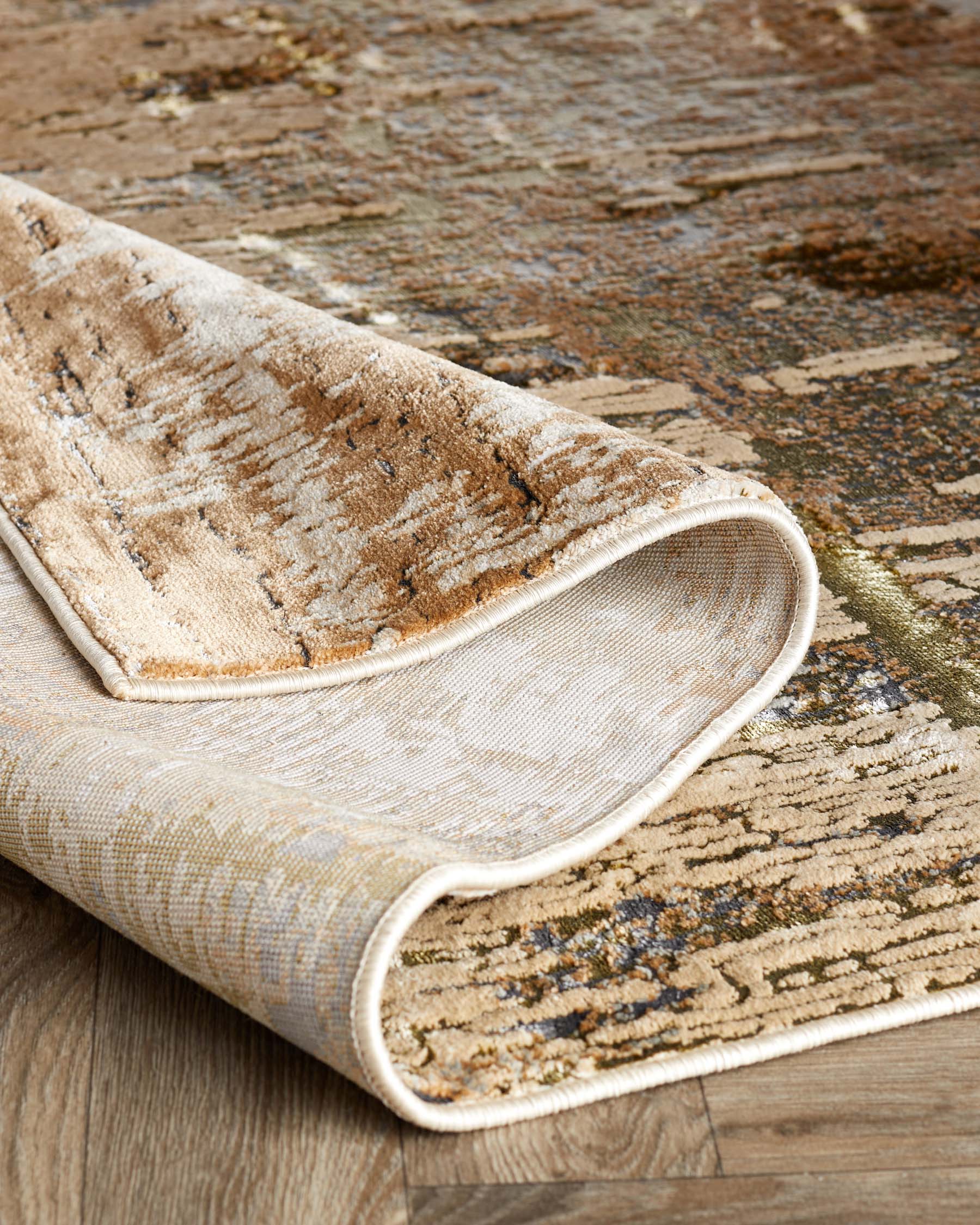 A textured, multi-tonal area rug featuring warm earthy colours with hints of green and blue accents, partially rolled to reveal its underside on a wooden floor.