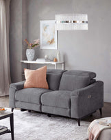 Gray upholstered couch with a blush pillow, modern pedestal table, decorative vase, and stylish pendant light above.