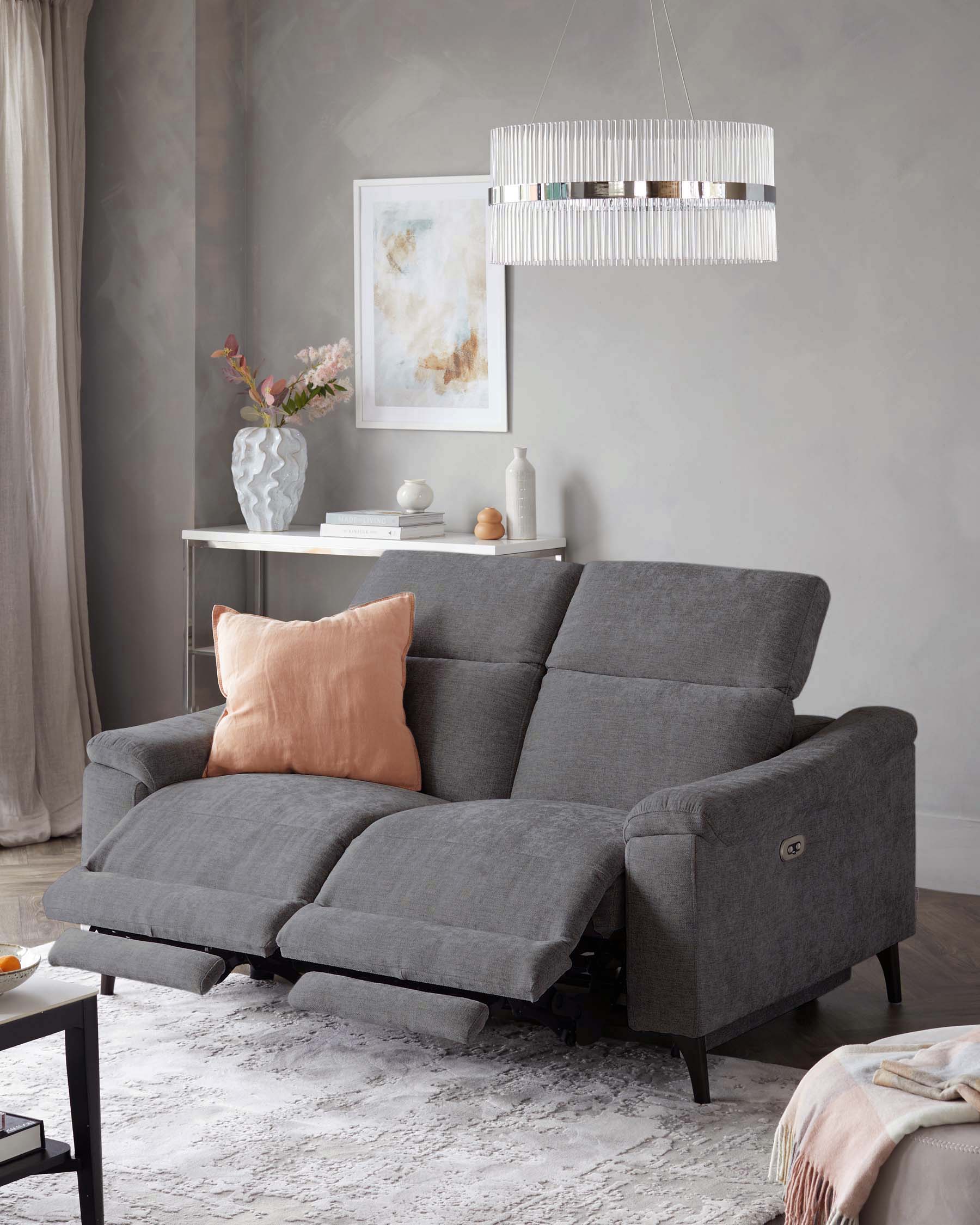 Gray reclining sofa with a plush cushion, accented by a pink pillow, paired with a minimalist side table and elegant lamp.