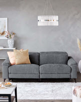 Gray upholstered sofa with plush cushions, a sleek coffee table, and a stylish pendant light above, set against a neutral wall.