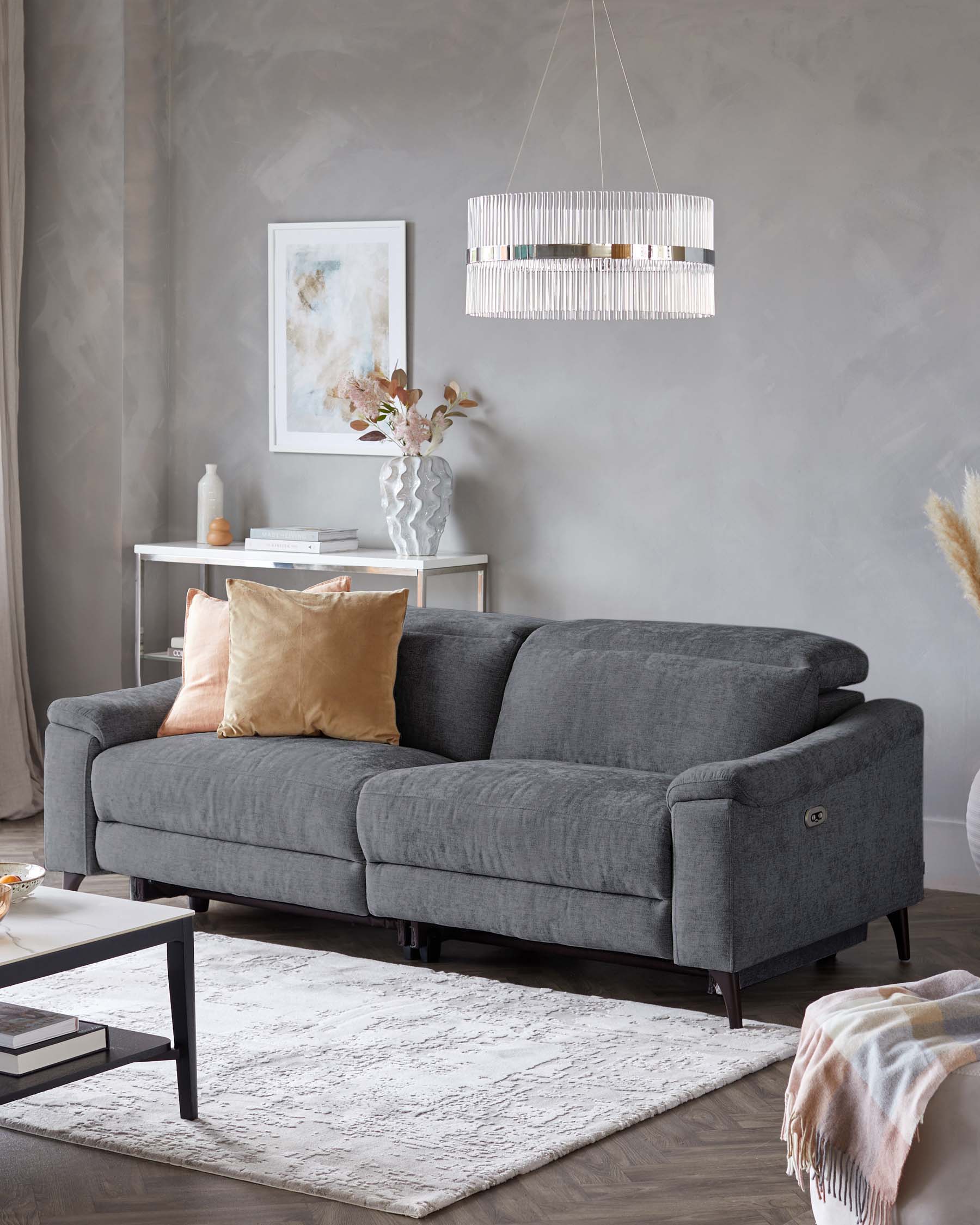 Gray plush sofa with decorative pillows, modern pendant light, stylish vase with flowers, and sleek coffee table on a textured rug.