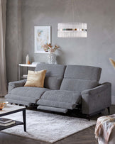 A gray reclining sofa with a gold cushion, paired with a black coffee table and a decorative rug, accented by a stylish light fixture.