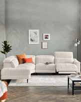 Modern light grey sectional sofa with a chaise on the left and a single-seater extension on the right, accented with an orange throw pillow. In front of the sofa is a rectangular black coffee table with a white tabletop, over a faded white and grey area rug.