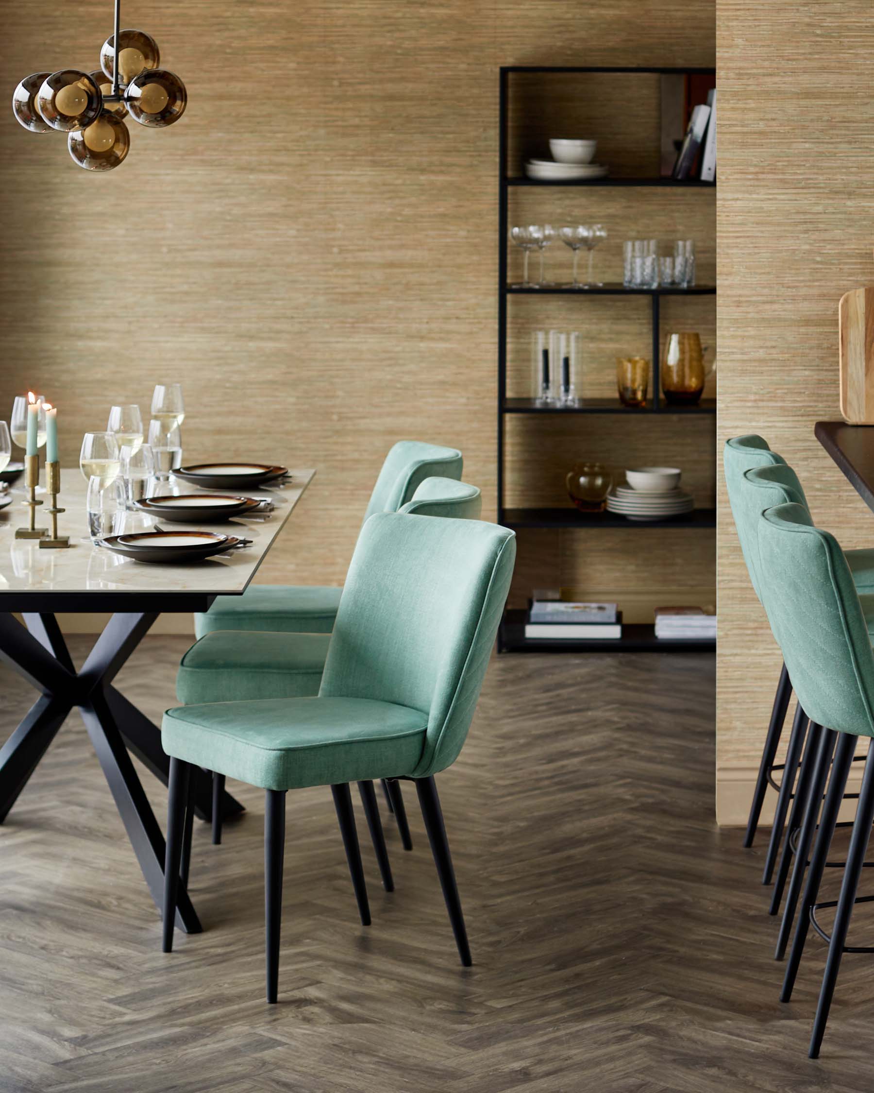 A modern dining setup with a glass table, mint green upholstered chairs, a stylish light fixture, and a sleek black shelving unit.