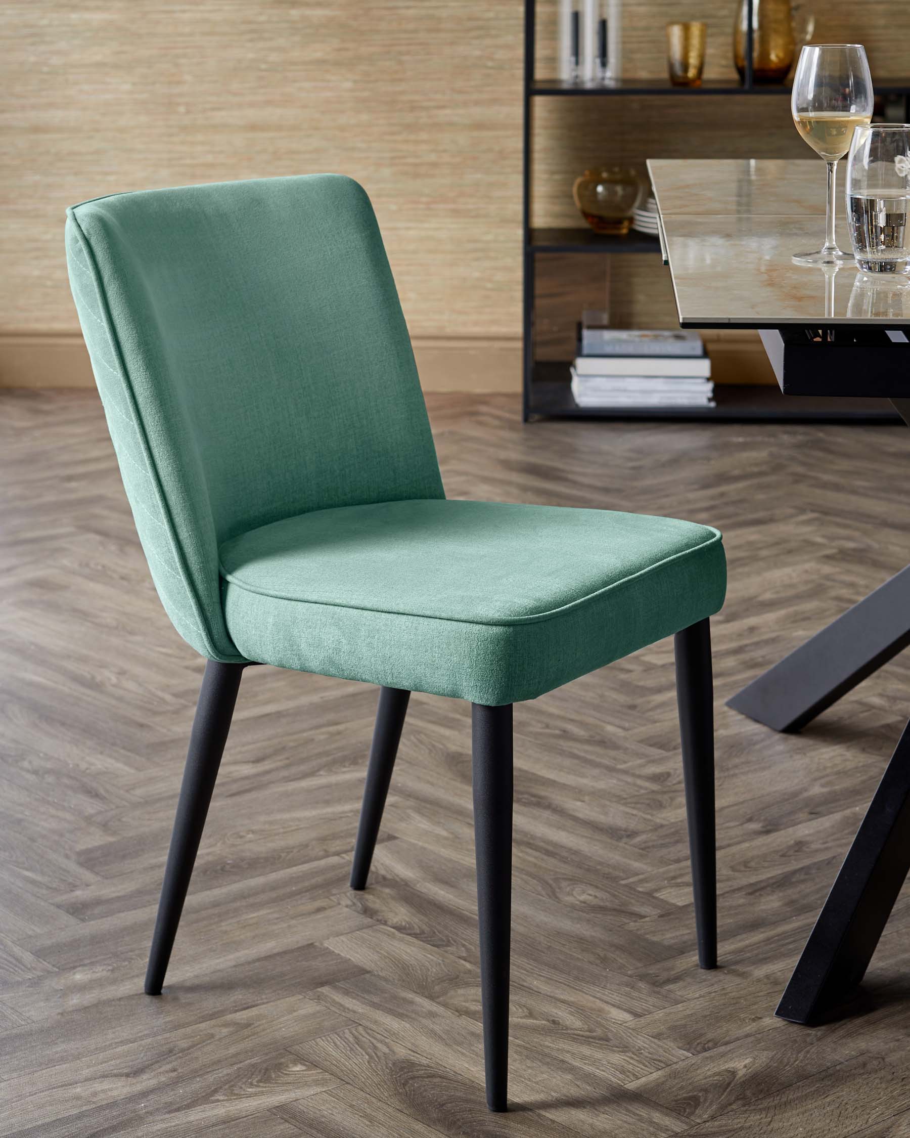 A modern green upholstered dining chair with sleek black legs, complementing a stylish dining space.