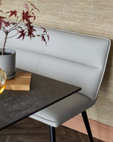 A sleek, modern dining chair with a light gray seat, paired with a dark stone table, accented by a decorative plant.