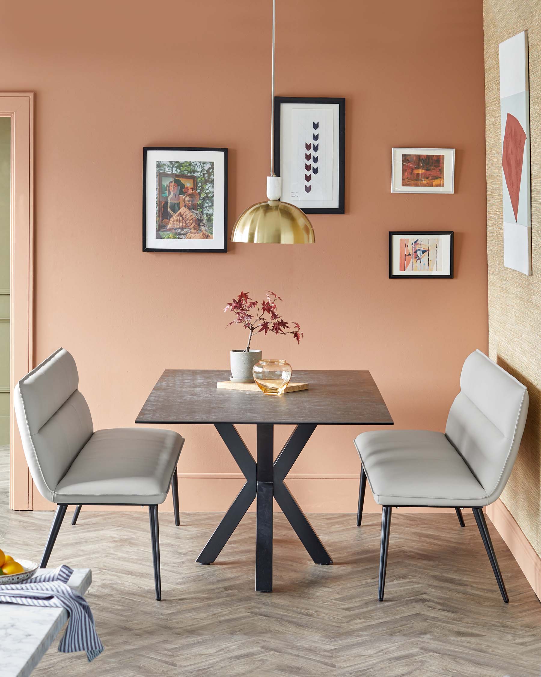 Stylish gray padded chairs paired with a modern square table featuring a black metal base, accented by a decorative light fixture.