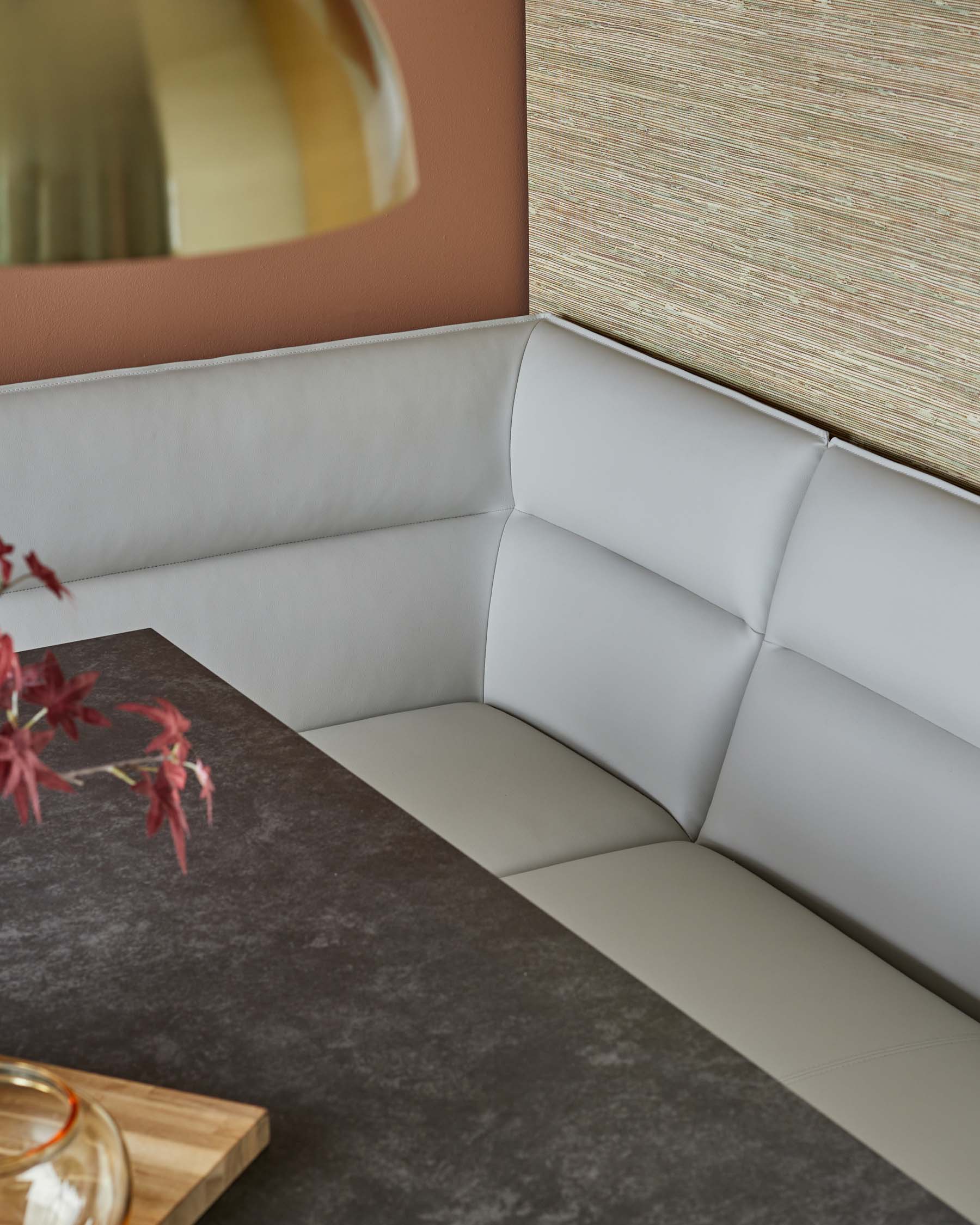 A sleek, padded light gray corner bench paired with a dark textured table, accented by a modern gold pendant light.