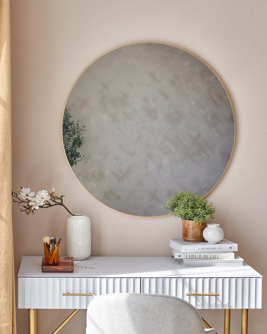 Elegant white console table with pleated skirt detail and brass handles, accompanied by a matching white stool with a plush cushion. A large round mirror with a thin golden frame hangs above, enhancing the sophistication of the set.