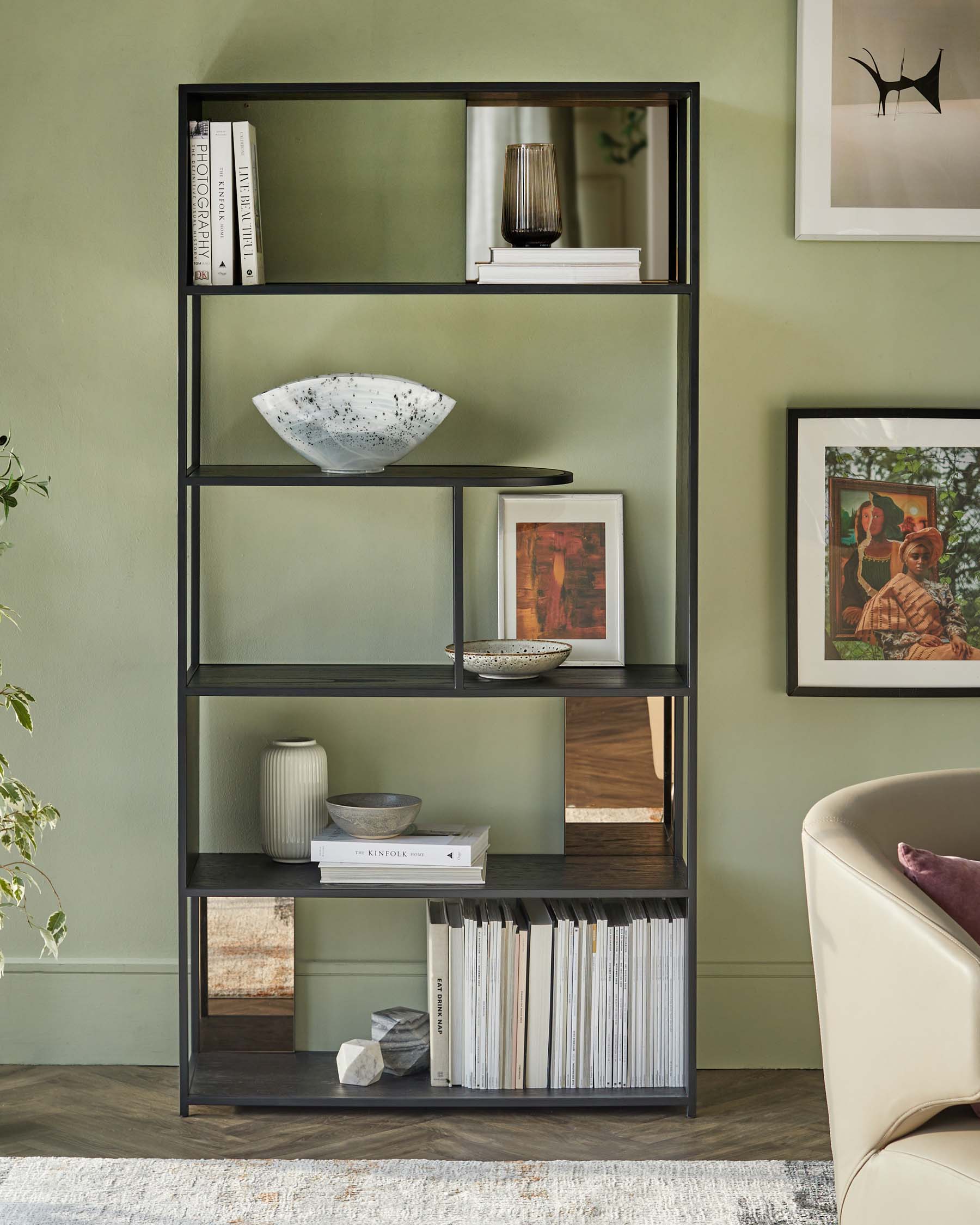 A sleek black shelving unit displays books, decorative bowls, and framed art against a soft green wall, enhancing a modern aesthetic.