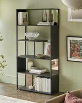 Stylish dark metal shelving unit displays books, decorative bowls, and vases against a soft green wall in a modern setting.