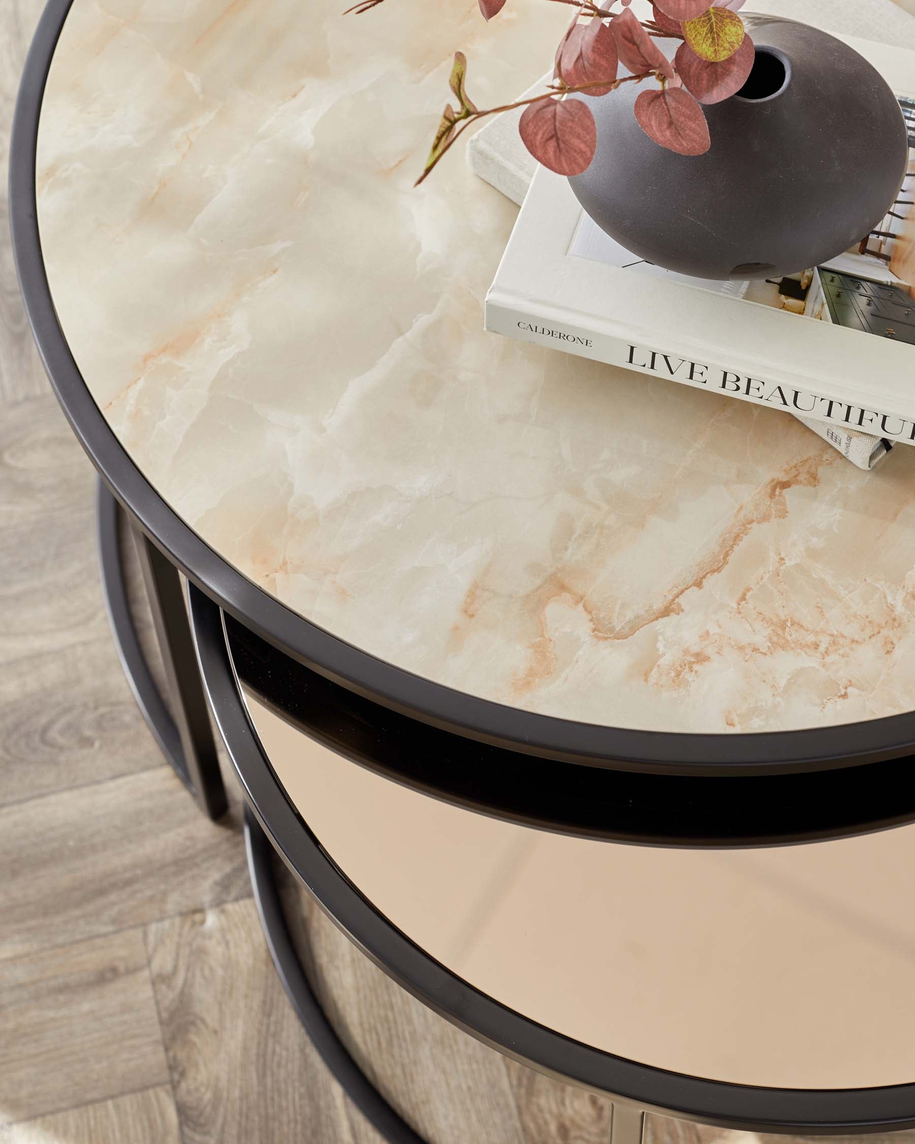 Elegant round side table with a marble-like tabletop design, featuring warm, creamy hues with subtle veining. The table is framed with a slim black edge and supported by a concentric circular matte black base, providing a modern and sophisticated look.