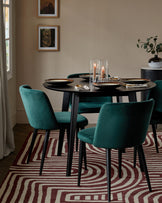 Round black dining table with stylish green velvet chairs and a decorative centerpiece, set against a patterned rug.