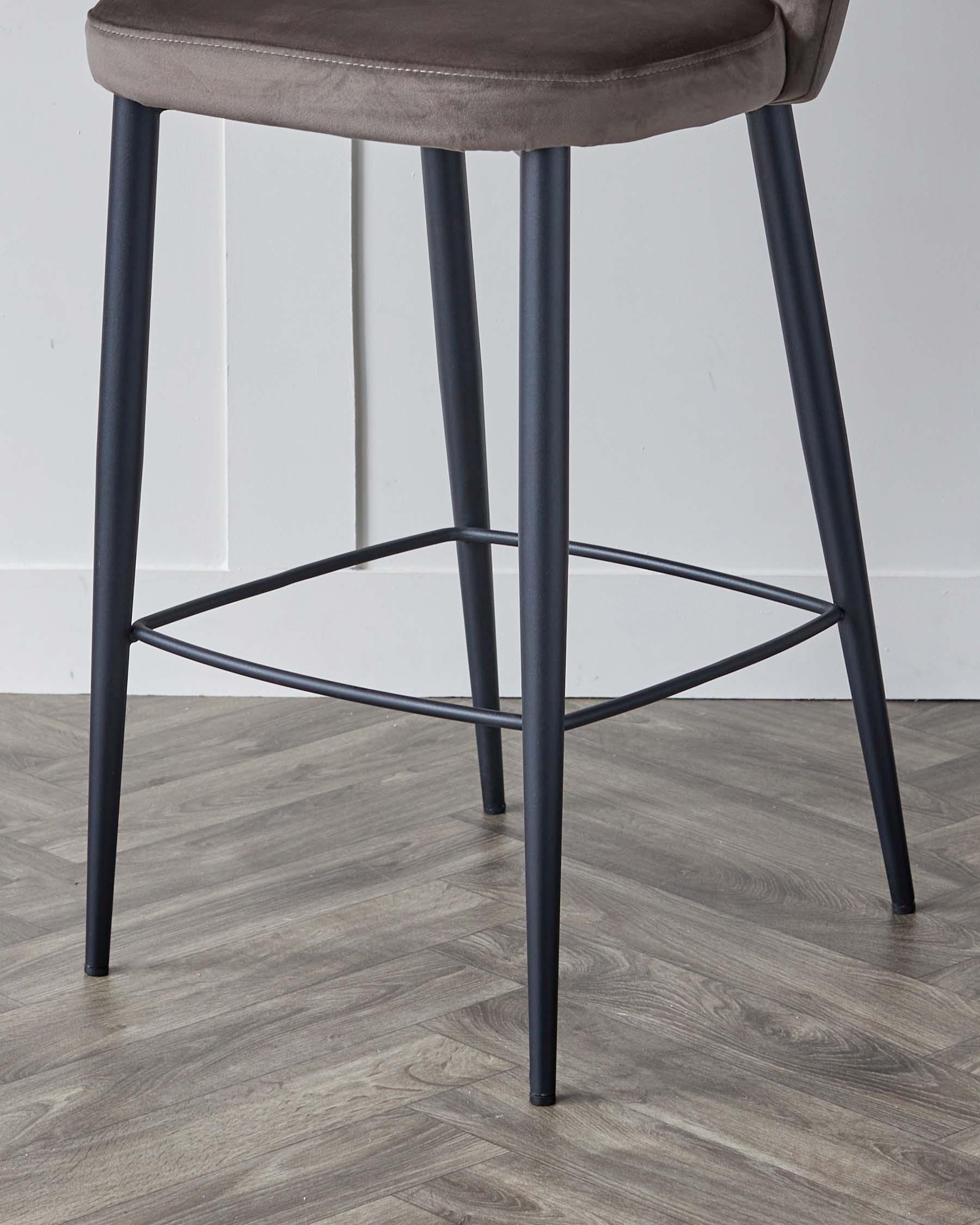 Modern bar stool with a grey upholstered round seat and slender matte black metal legs, featuring a geometric footrest design.