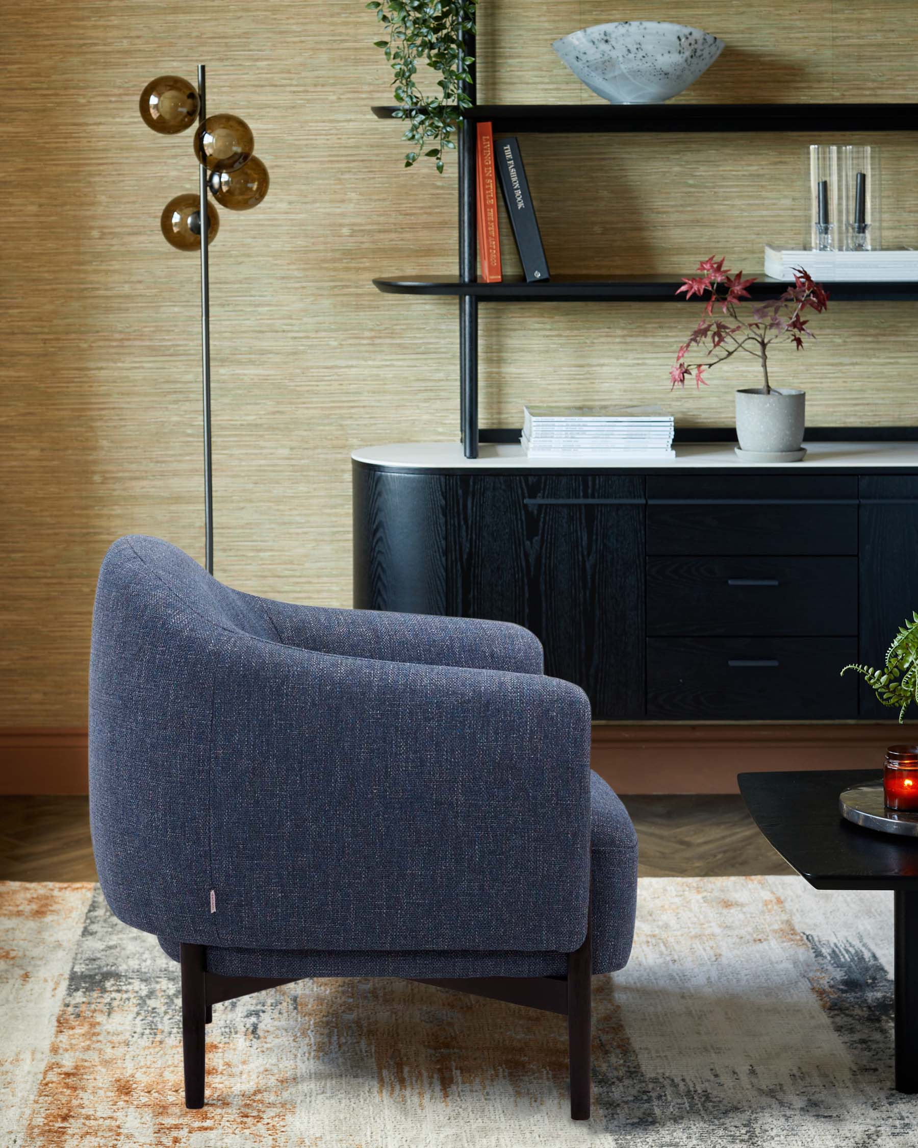 A modern blue upholstered armchair, sleek black shelving unit, a round table, and decorative accessories on a textured rug.