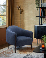 A cozy blue upholstered armchair with wooden legs, paired with a modern floor lamp and stylish accent table in a warm setting.