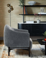 A plush gray armchair, sleek black shelving with decor, and a low black coffee table on a textured area rug.