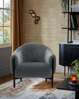 A stylish gray upholstered chair with rounded edges, paired with a modern floor lamp and black furniture accents.