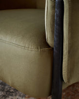 A close-up of a soft olive green fabric armchair, featuring a sleek black metal frame.