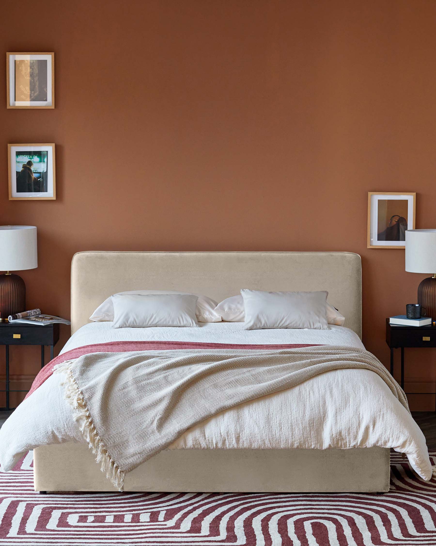 Minimalist bedroom with a plush beige bed, two stylish lamps, and a patterned rug, complemented by modern wall art.