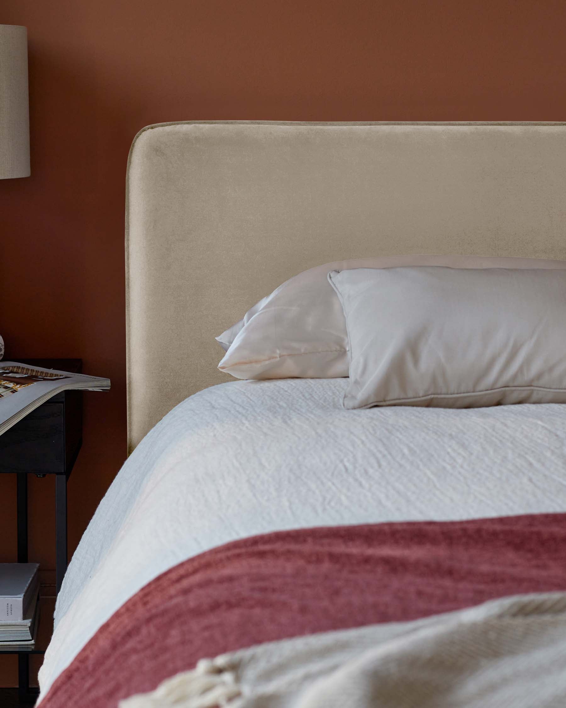 Elegant bed with a velvet headboard, layered pillows, and a textured blanket, complemented by a sleek nightstand and lamp.