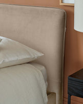 Velvety beige headboard paired with soft bedding, complemented by a sleek black nightstand and elegant lamp.