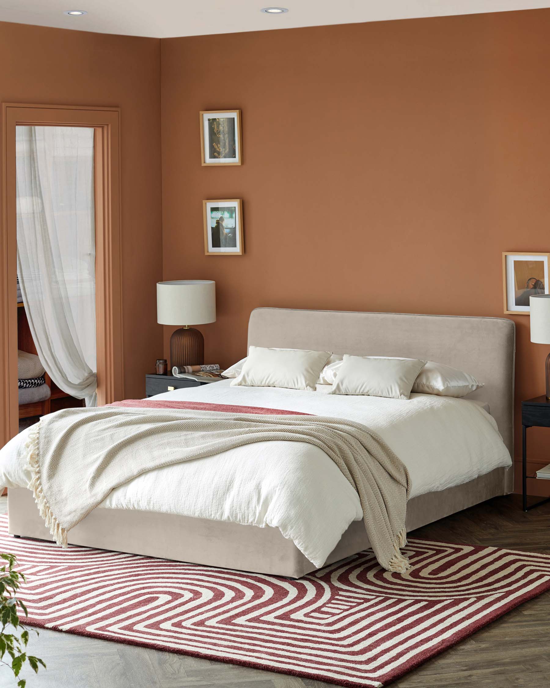 Modern bedroom featuring a plush bed with neutral bedding, stylish lamps, and a patterned rug on hardwood flooring.