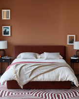 Cozy bedroom with a deep red upholstered bed, layered blankets, bedside tables, stylish lamps, and a patterned rug.