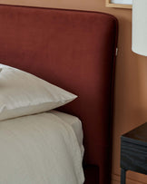 Luxurious rust-colored upholstered headboard with soft bedding and a sleek black nightstand beside a stylish lamp.