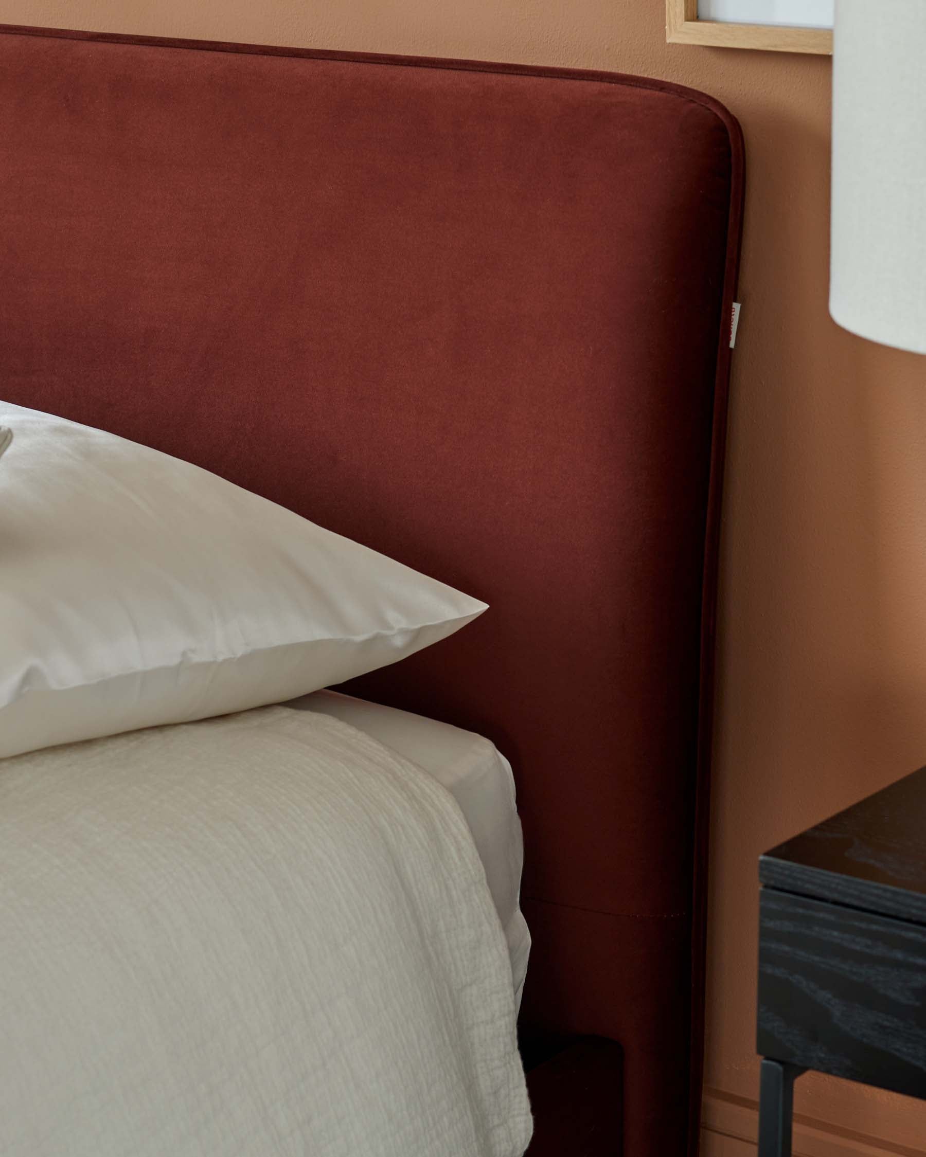 Luxurious rust-colored upholstered headboard with soft bedding and a sleek black nightstand beside a stylish lamp.