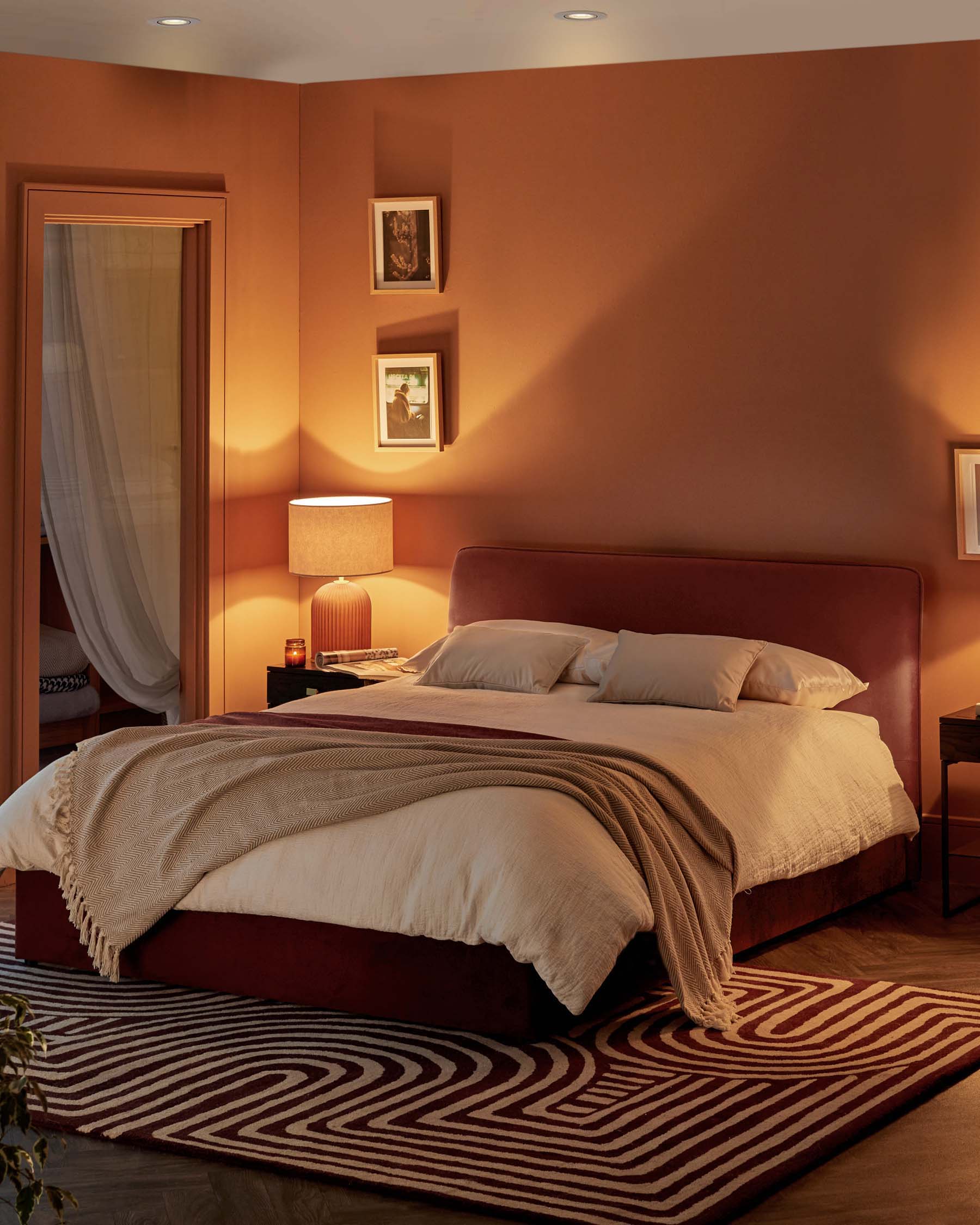 Chic bedroom featuring a padded bed with neutral bedding, a textured throw, a stylish lamp, and a patterned area rug.