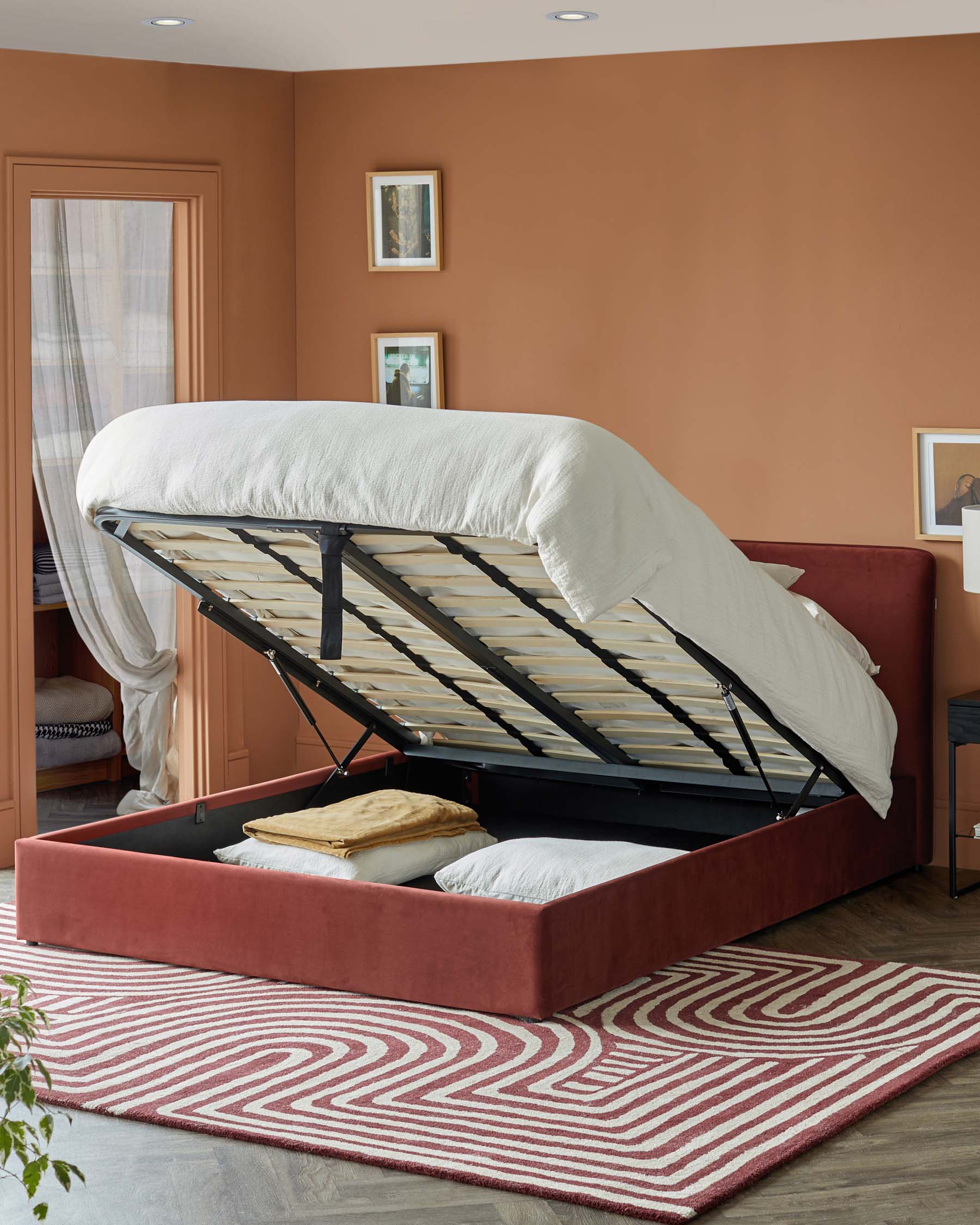 A modern, burgundy upholstered bed with a hydraulic lift for storage, complemented by a patterned rug on a wooden floor.