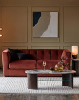 Plush rust-colored sofa, round marble-top coffee table with wood base, cozy accent rug, and stylish lamp in a warm-toned interior.