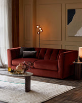 A plush burgundy sofa with accent pillows, a glass top coffee table, a stylish floor lamp, and decorative accessories on a rug.