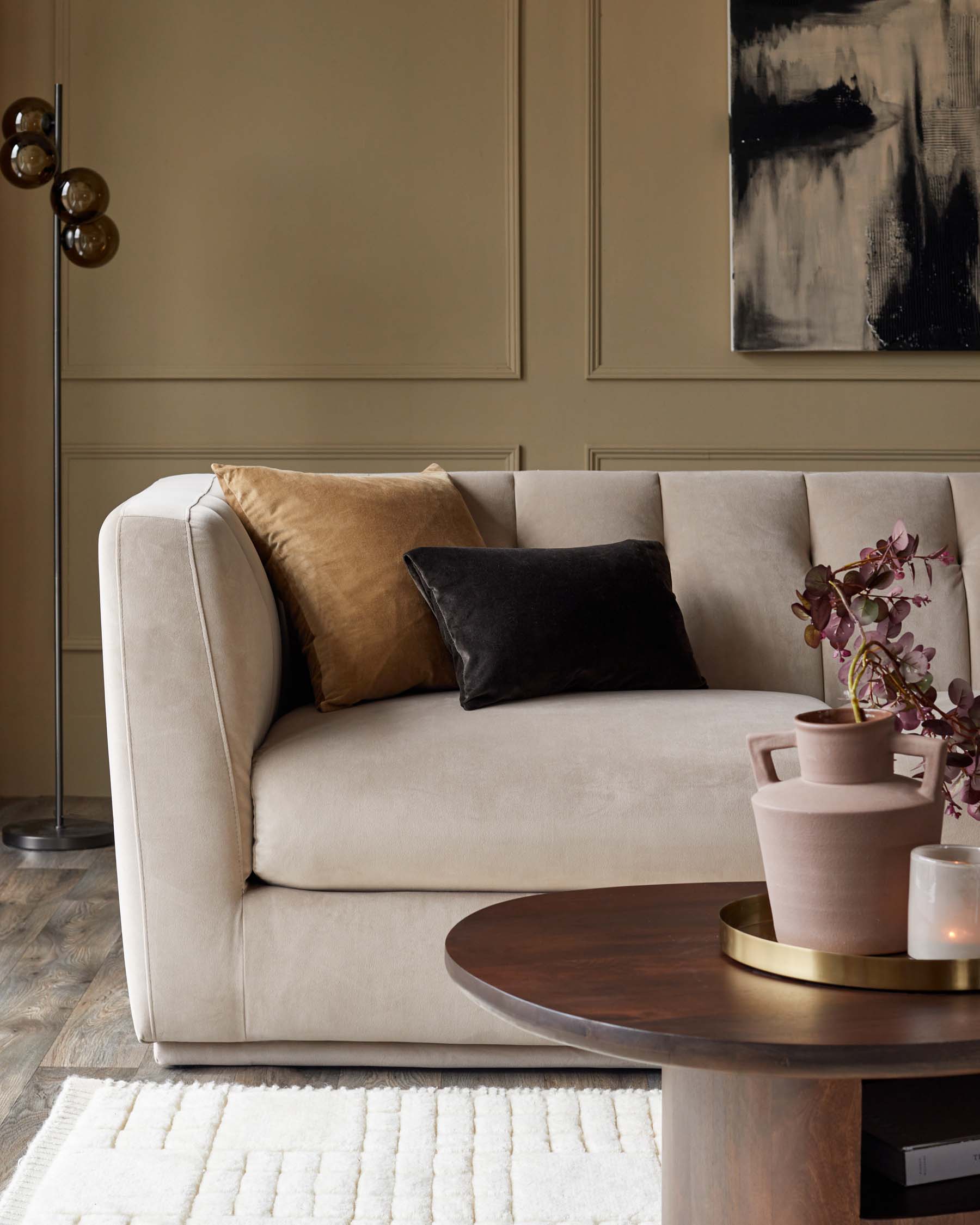 Elegant beige sofa with colorful cushions, round wooden coffee table, and minimalist decor, set against a textured wall.