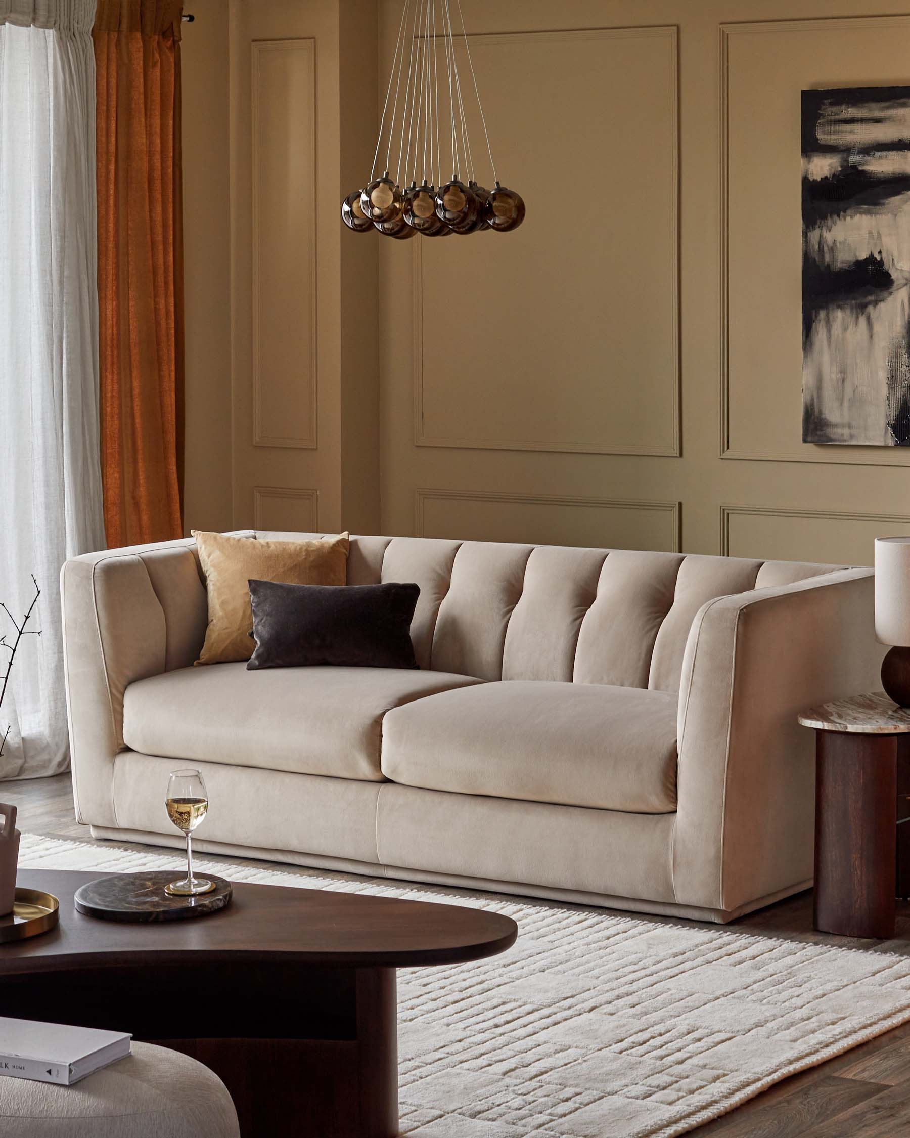 A plush beige sofa with tufted design and decorative pillows, a sleek dark wood coffee table, and elegant hanging pendant lights.