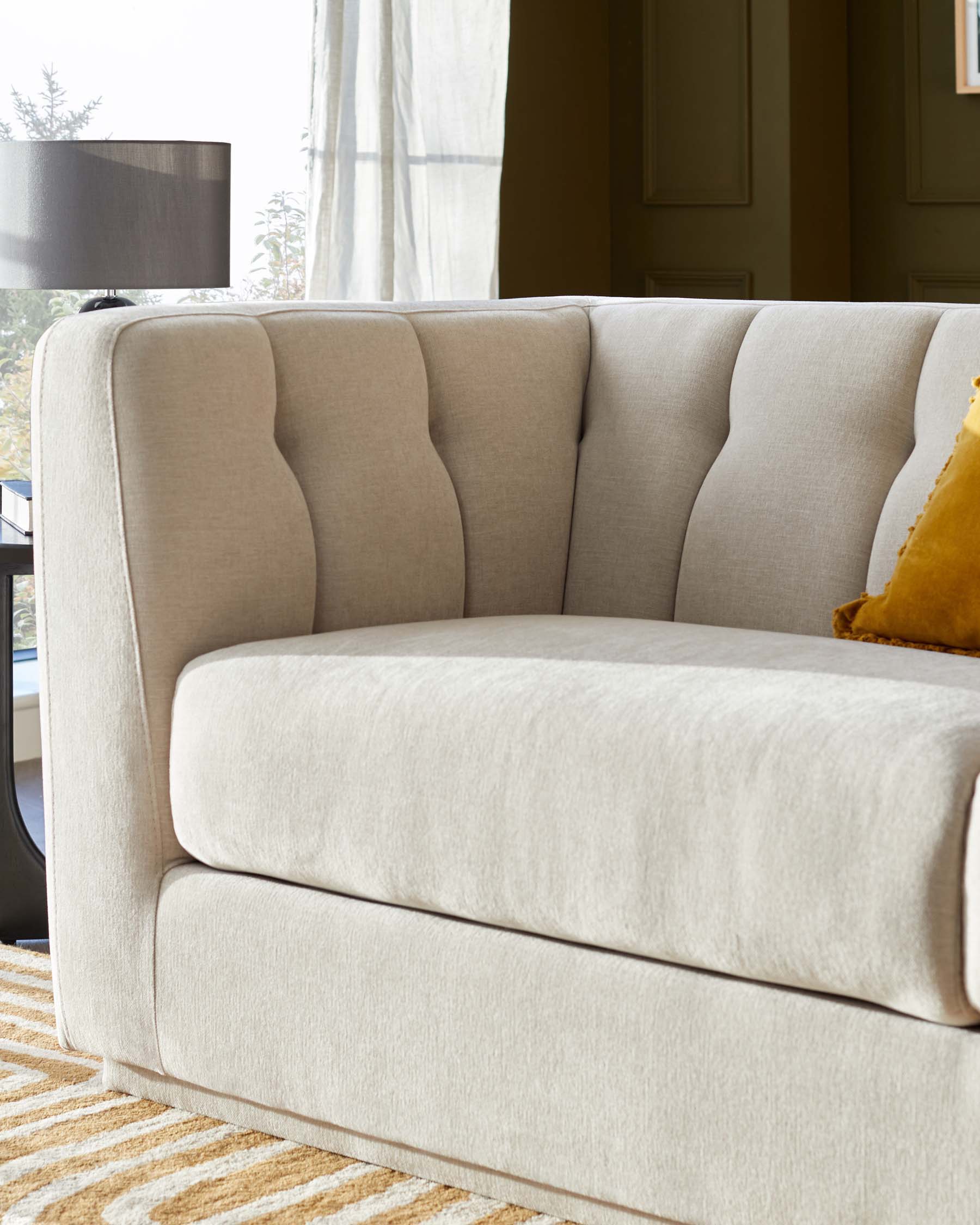 A plush, cream-colored couch with tufted backrest, paired with a decorative yellow pillow, set against a cozy room backdrop.