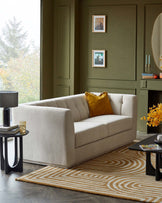 A modern light-colored sofa with tufted back, patterned area rug, sleek side table with lamp, and a low black coffee table.