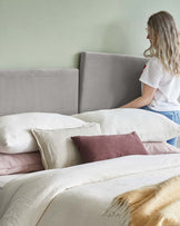 Gray upholstered headboards frame a layered bed with white, cream, and brown pillows, topped with a soft, fringed blanket.