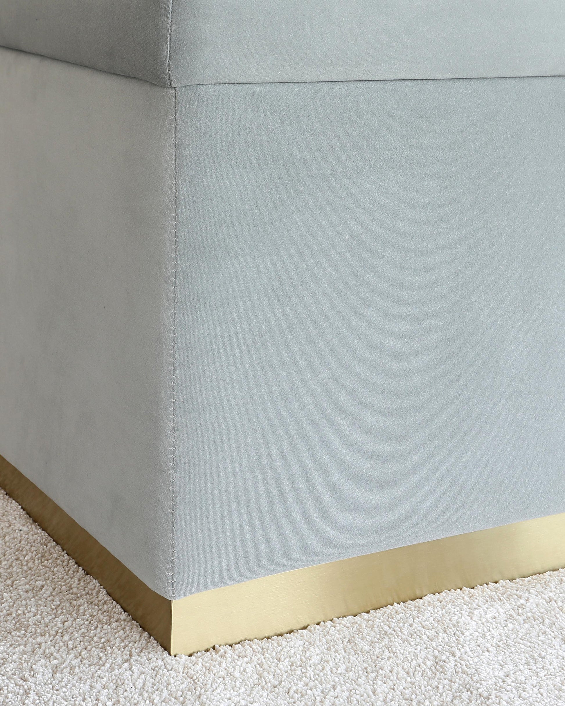 A sleek, upholstered piece in soft gray with a stylish gold base, resting on a plush carpet.