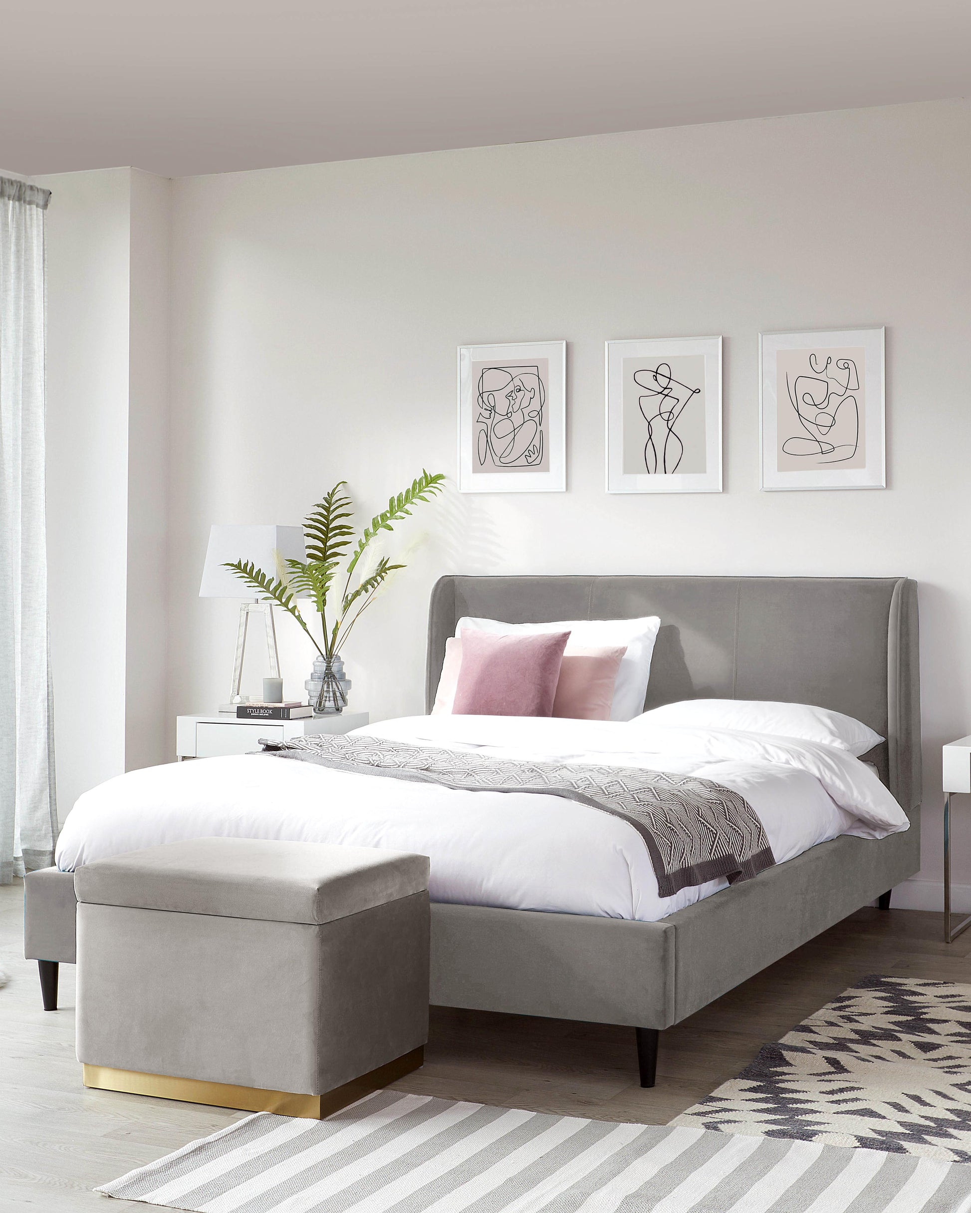 Stylish grey upholstered bed with a matching ottoman, accent pillows, minimalist nightstand, and decorative wall art.