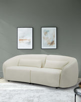 A stylish, cream-colored upholstered sofa with rounded edges and two back cushions, complemented by abstract wall art.